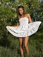 Enchanting teen with an innocent look taking off white dress and posing naked in the nature.