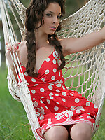 With curly hair in loose braids, wearing red and white polka dotted dress among lush green grass, melany evokes a sweet and young maiden, her petite b