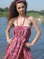 Charming dainty teen with long brown curly hair makes up to entertain a little bit alone on the deserted beach of the blue river.