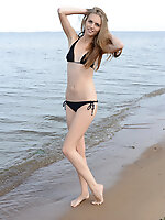 Winsome long haired teen cutie taking off clothes and showing appetizing body on the shore.